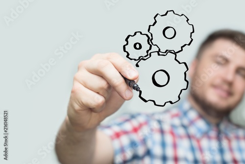 Man with black marker draws on a transparent board or glass wall. Gear wheel of mechanism.