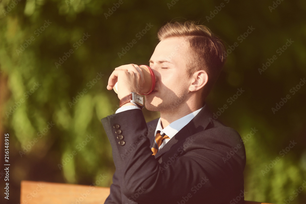 Young man in formal clothes drinking cup of coffee in park on sunny day Young man in formal clothes drinking cup of coffee in park on sunny day