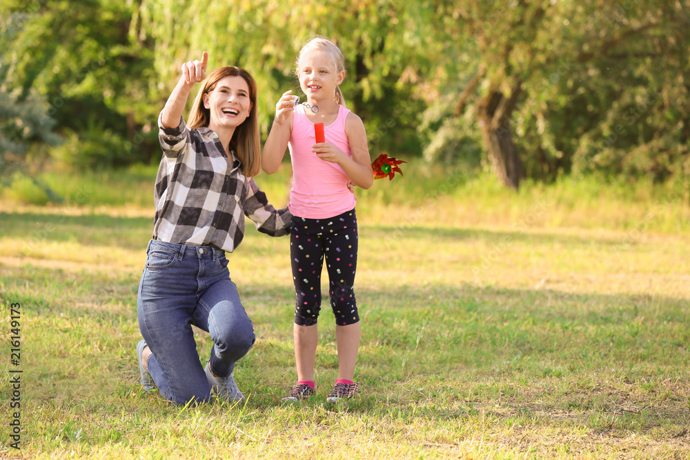 Fototapeta premium Woman and her daughter blowing soap bubbles in park