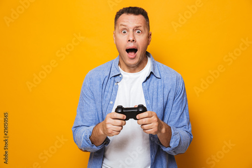 Emotional man isolated over yellow background play games with joystick.