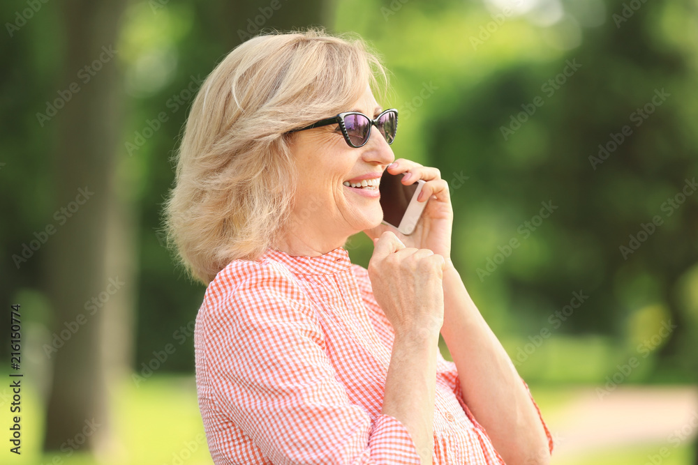 Fototapeta premium Beautiful mature woman talking on mobile phone outdoors