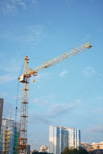 concrete building and yellow tower crane against blue sky background