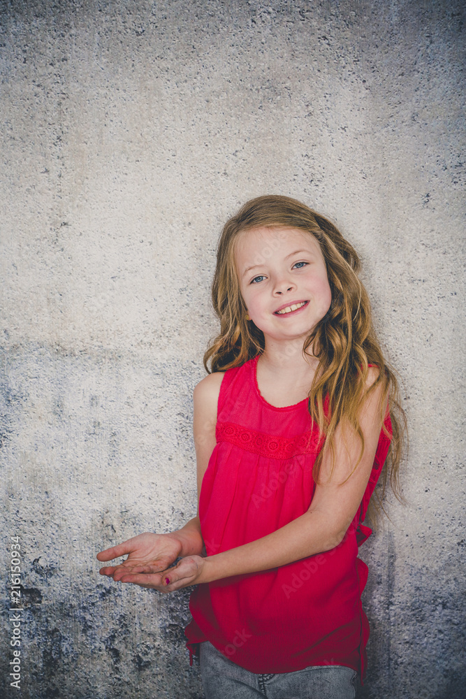 beautiful girl in red shirt in front of concrete background is posing and pointing beautiful girl in red shirt in front of concrete background is posing and pointing