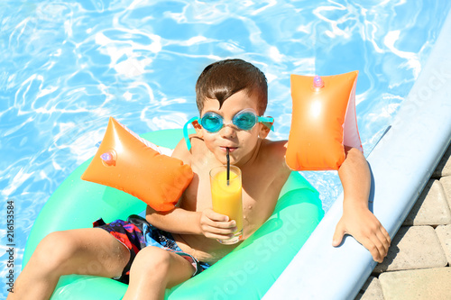 Cute little boy with inflatable ring drinking juice in swimming pool