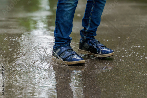 Child legs in sneakers close-up, the child jumps in puddles. Health, happy childhood concept.