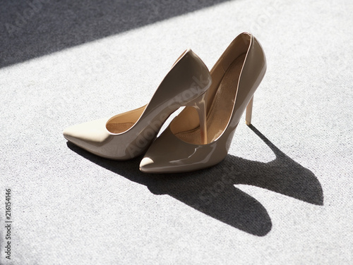 Close-up of a Pair of nude high heel stiletto shoes and their shadow on a grey floor