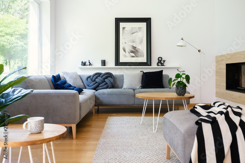 Poster on white wall in living room interior with table in front of corner sofa with pillows. Real photo