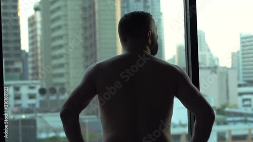 Toples man standing in his apartment and admiring the view from the window
 photo