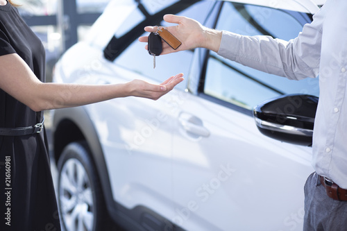 Close-up of seller's hands with keys and buyer after transaction in car showroom