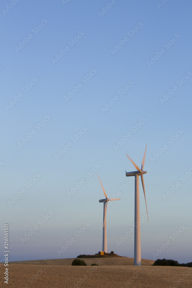 Wind turbines at a field for agriculture in the island of Jylland, Denmark. Rolling hills at dusk.