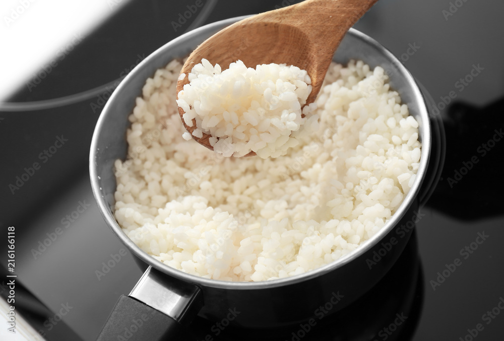 Spoon with boiled rice over saucepan on stove, closeup