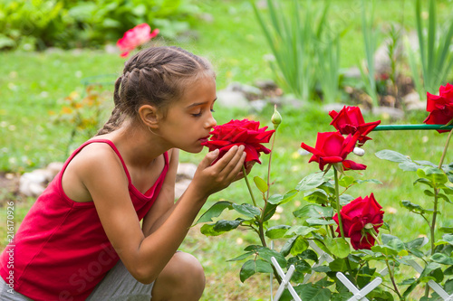 Little girl smelling beautiful red roses in a summer garden
