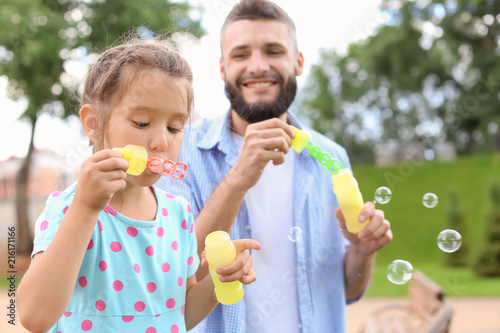 Little girl and her father blowing soap bubbles outdoors