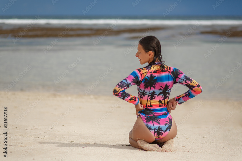 Beautiful girl in swimsuit sitting on white sand beach and lookin forward Beautiful girl in swimsuit sitting on white sand beach and lookin forward