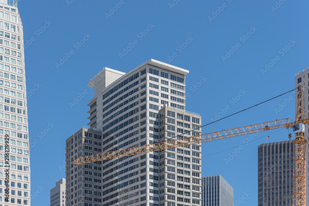 Working yellow crane near completed building in downtown San Francisco, California, USA. Construction and industrial background office and residential skyline, clear blue sky