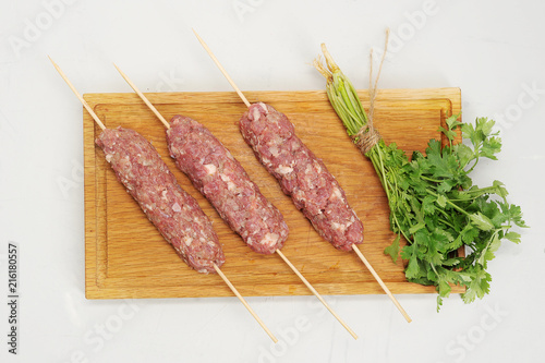On a wooden board the kebab lulia on wooden skewers. Kebab of minced meat. A bunch of fresh coriander is near. White background. Close-up. View from above. photo