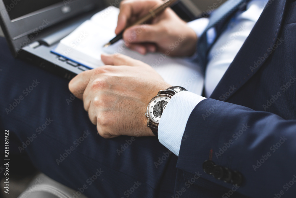 Man in a business suit write on notebook with laptop in the car