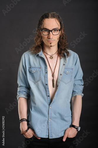 Young handsome boy in denim shirt and glases, curly hair, hands in pockets