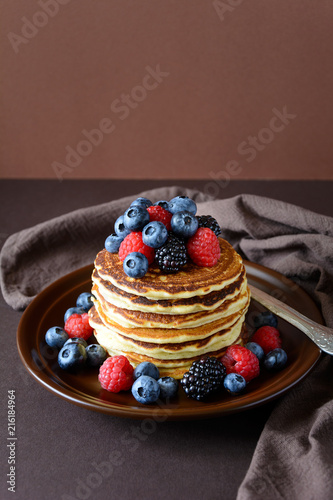 Stack of pancakes with fresh blueberry, raspberry and blackberry on brown plate