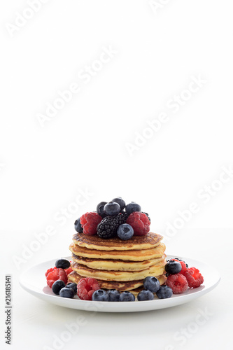 Stack of pancakes with fresh blueberry, raspberry and blackberry on white plate
