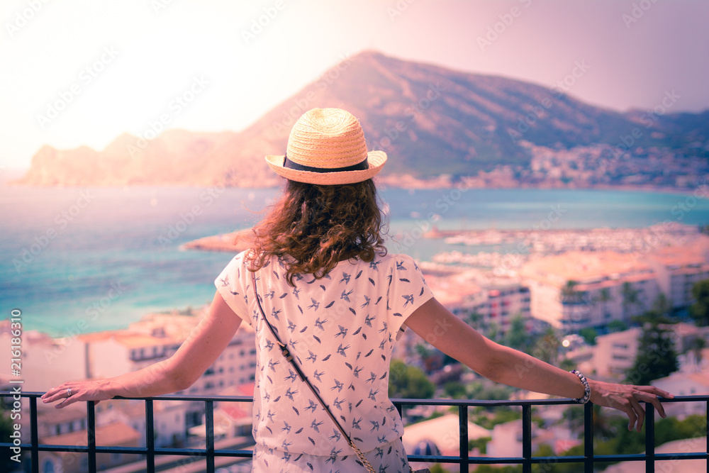 Tourist woman with straw sunhat looking to the mediterranean sea and enjoying the blue and scenic seascape in Altea, Alicante, Spain