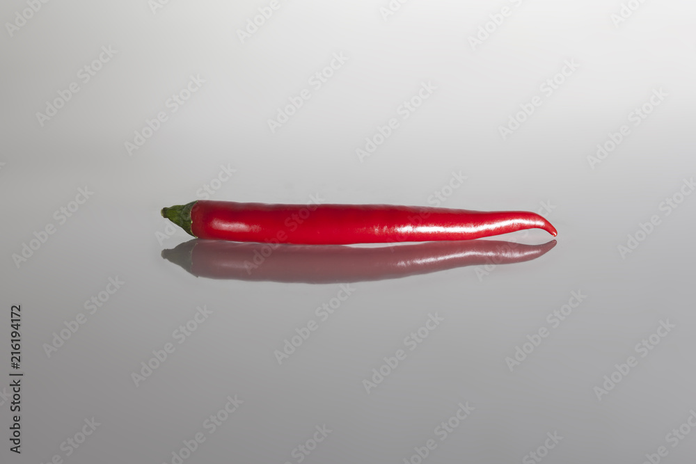 Red color hot chilli pepper as ingredient of spicy meal or salad on reflecting neutral surface
