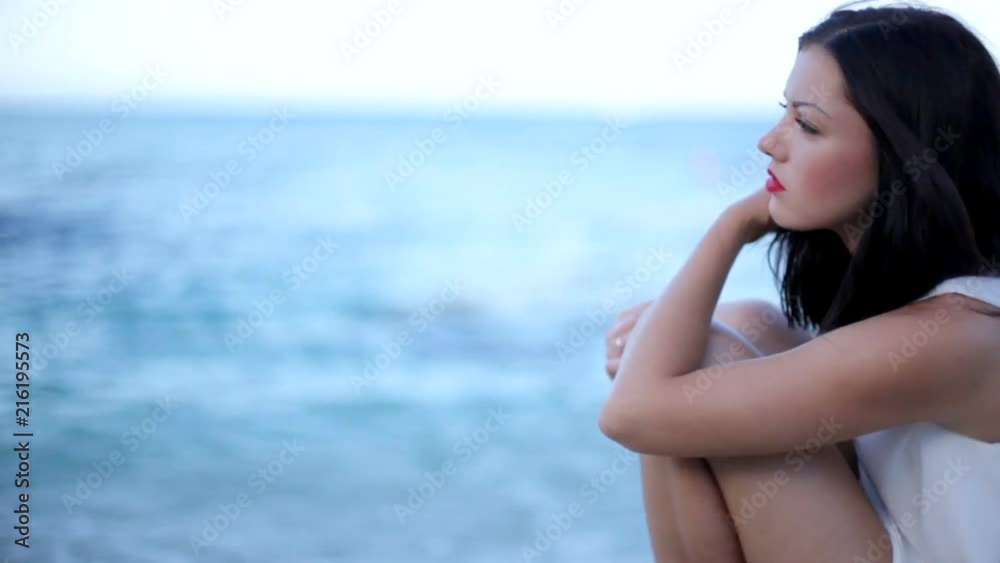Beautiful girl close-up looks at the camera. emotional face on the beach. sad girl is sitting by the sea.