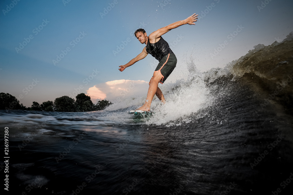 Active young man riding down the river waves in evening