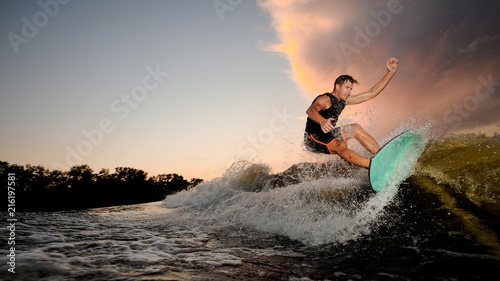 Handsome muscular young man wakesurfing down the river waves