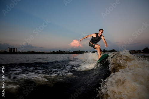 Handsome muscular man riding on wakesurf down the river during sunset