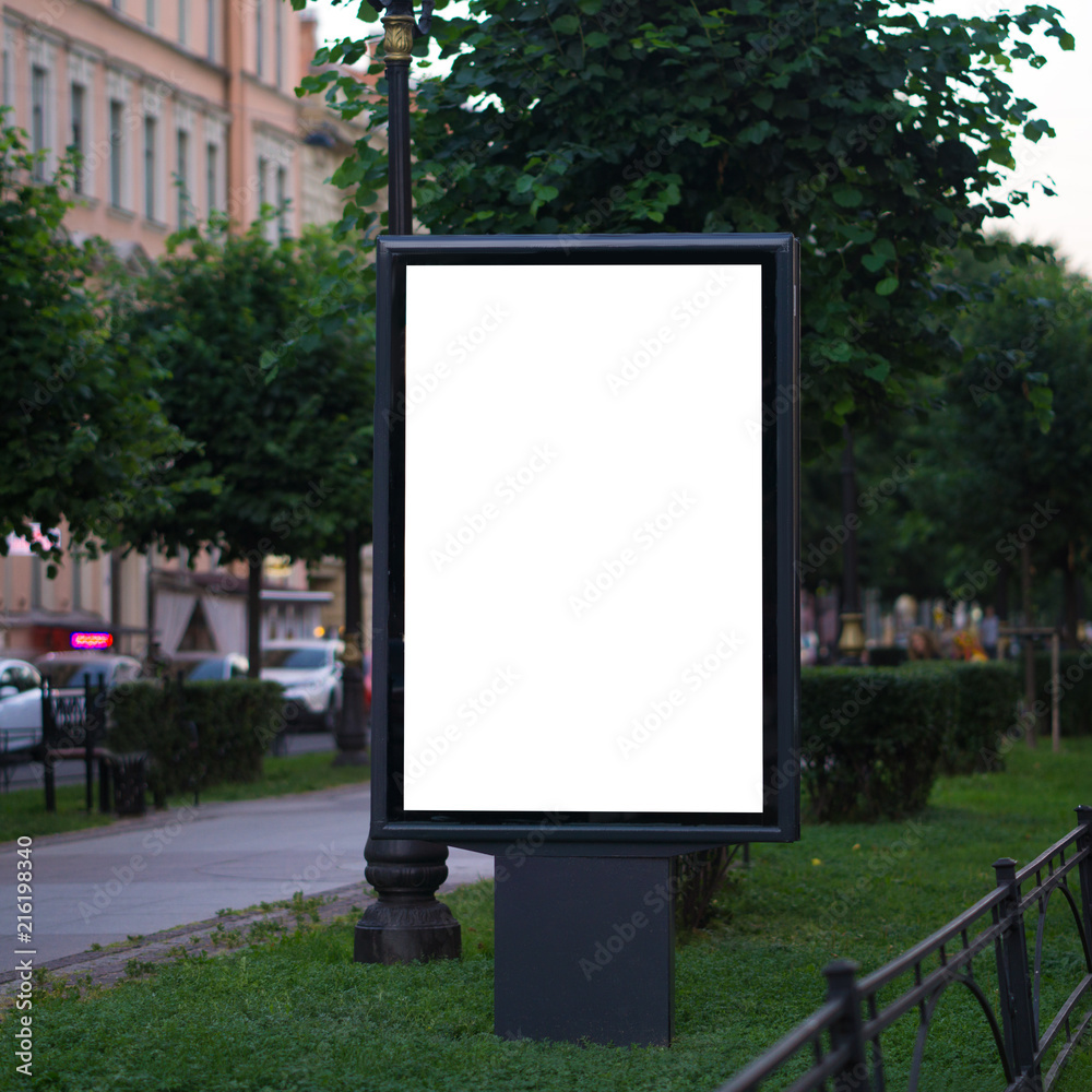Fototapeta premium light poster billboard standing in the street in the summer. layout for advertising white. Vertical blank glowing billboard on the city street Mock up