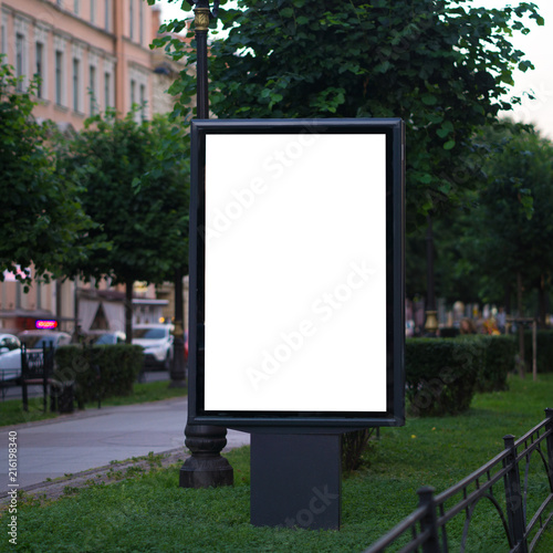 light poster billboard standing in the street in the summer. layout for advertising white. Vertical blank glowing billboard on the city street Mock up
