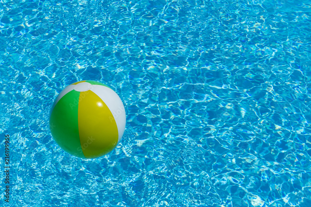 Inflatable multicolored ball floating on swimming pool water, with copy space, summer recreation concept.