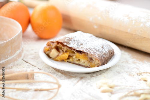 strudel (roll strudel) with orange on a wooden board with flour