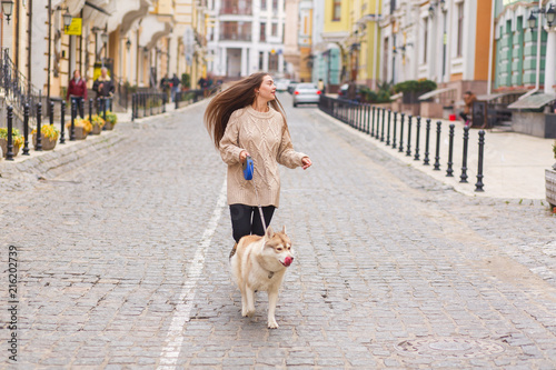 The woman take a walk with husky dog at sunny autumn day on old European city street. Horizontal view
