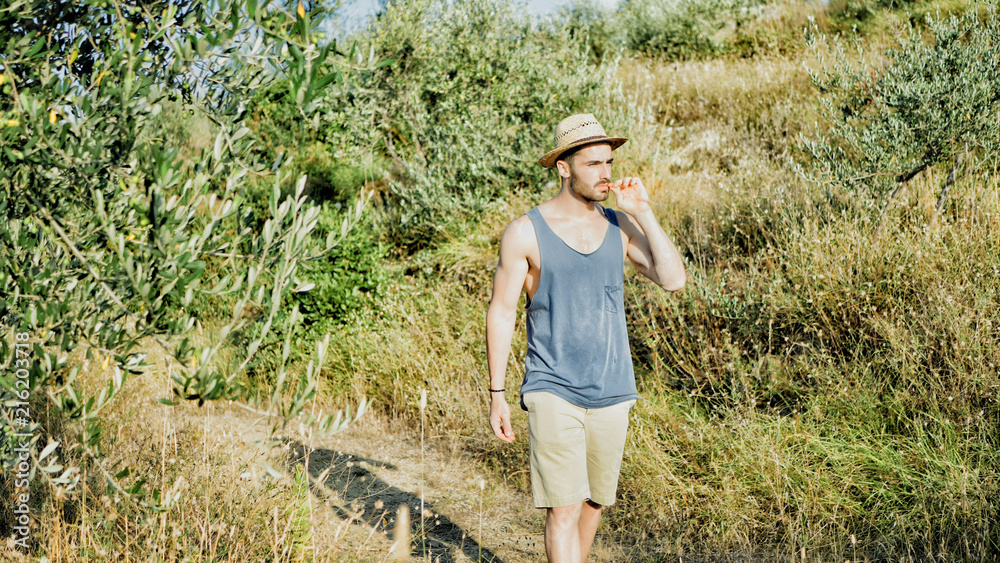 Attractive, fit young man relaxing walking in a grass field, wearing straw hat