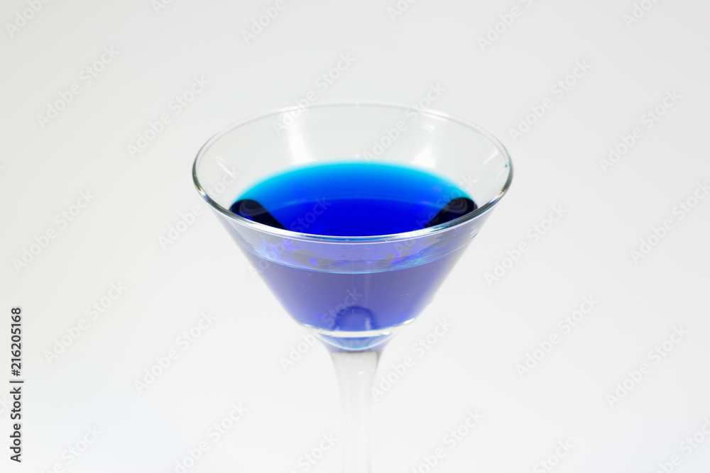 Halloween inspired blue color cocktail in a clear glass sitting on a white table waiting to be enjoyed.
