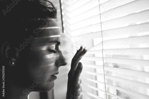 Depressed young woman near window at home, closeup photo
