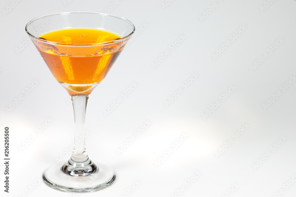 Halloween inspired orange color cocktail in a clear glass sitting on a white table waiting to be enjoyed.