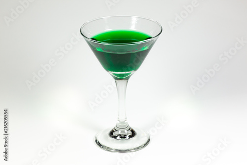 Halloween inspired green color cocktail in a clear glass sitting on a white table waiting to be enjoyed.