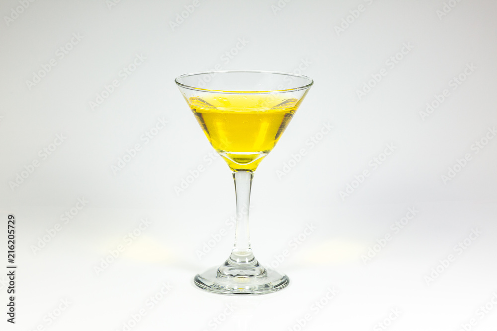 Halloween inspired yellow color cocktail in a clear glass sitting on a white table waiting to be enjoyed. Halloween inspired yellow color cocktail in a clear glass sitting on a white table waiting to be enjoyed.