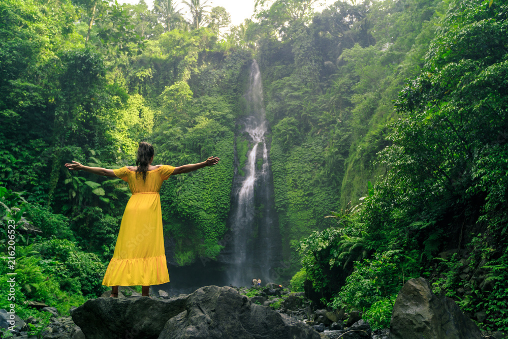 Fototapeta premium Woman in yellow dress at the Sekumpul waterfalls in jungles on Bali island, Indonesia