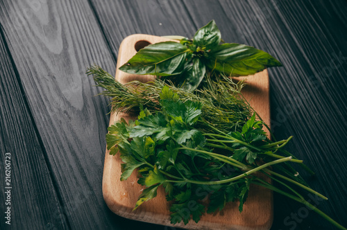 Herbs and spices on a wooden brown board, on a black wooden background. Parsley dill. Ingredients for cooking. Top view, a metso under the text photo