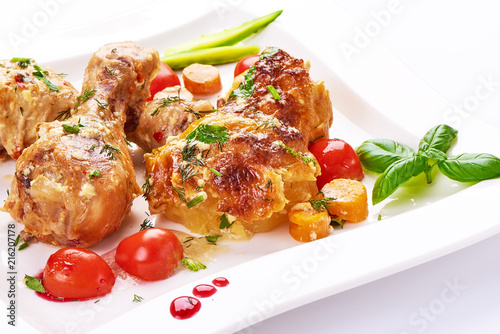Roasted chicken legs with baked potatoes and vegetables, isolated on white background.