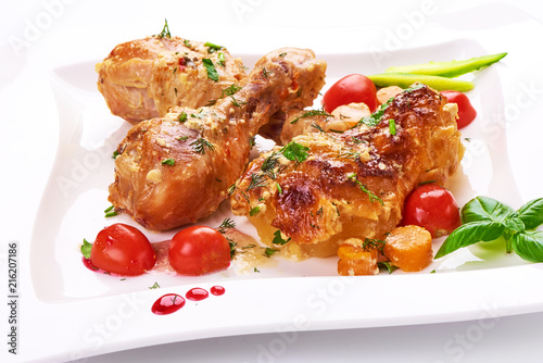 Roasted chicken legs with baked potatoes and vegetables, isolated on white background.