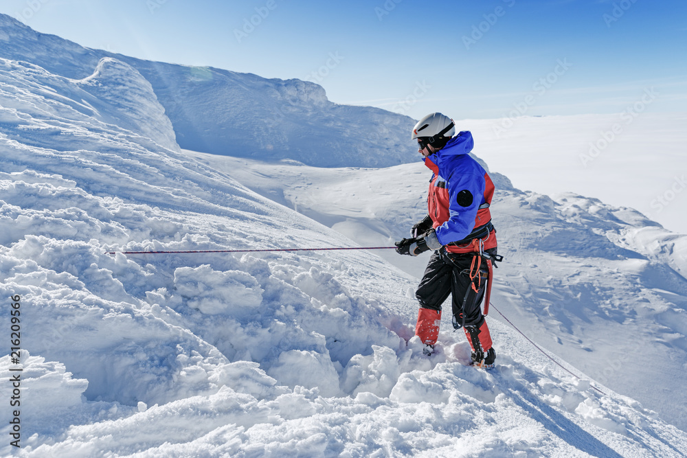 Brave male climber moving by snowy slope by rope. Extreme activity concept.