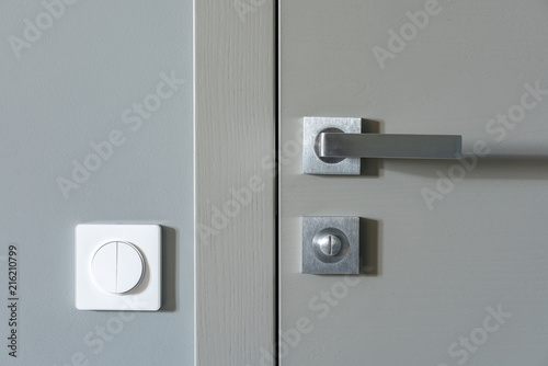 A metal handle and a lock on the gray interior door and a white switch on the gray wall. Element of apartment design.