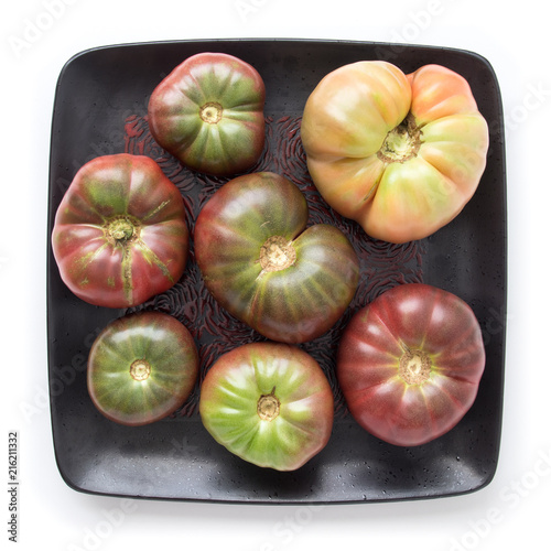 Organic heirloom tomatoes on a black square plate, isolated on white, top view photo