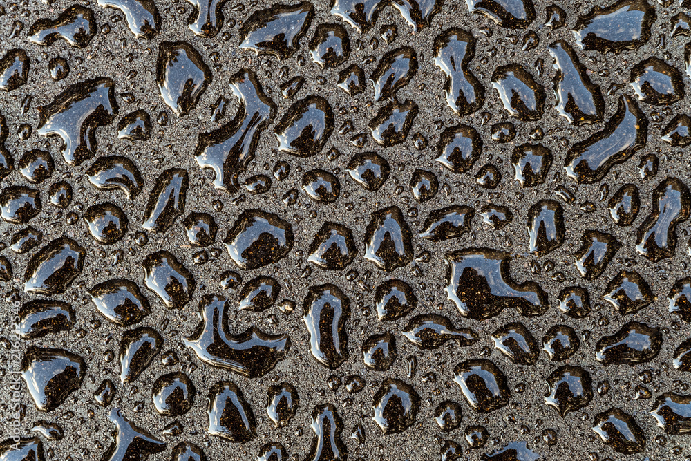 Water drops on a smooth gray surface close-up. Abstract background. Fresh drops of on a dark asphalt.