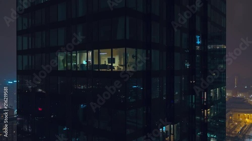 The drone flies up a modern, glazed skyscraper in which the lights of the night Warsaw are reflected.
